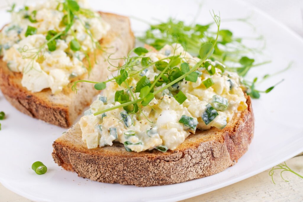 Patê de ovos servido em fatia de pão em prato de cerâmica branco em cima de mesa