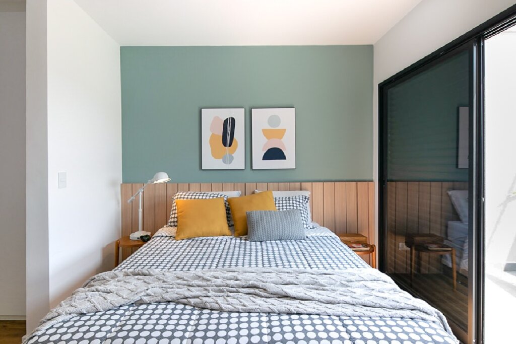 Dormitório com cama centralizada, cabeceira ripada de madeira, parede verde e portas de vidro laterais