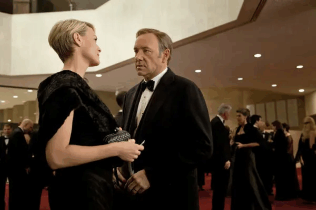 A imagem mostra dois personagens da série House of Cards, um homem e uma mulher, inseridos em um contexto de evento formal e alta sociedade, típico do universo político retratado na produção
