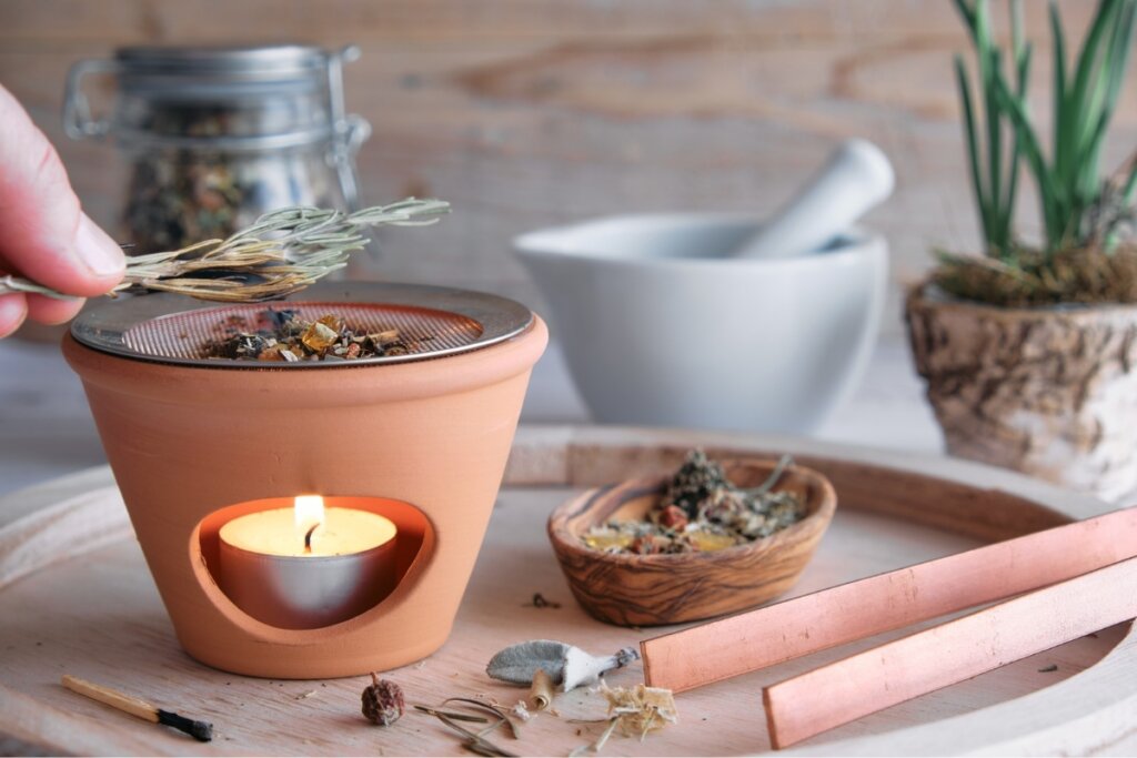 Recipiente marrom com folhas de alecrim queimando em uma vela