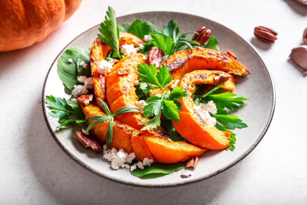 Prato branco com salada de abóbora, queijo cottage, nozes e folhas verdes 