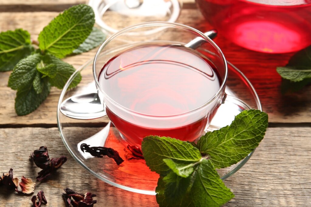 Chá de hibisco com hortelã em xícara de vidro transparente em cima de pires com folhas de hortelã