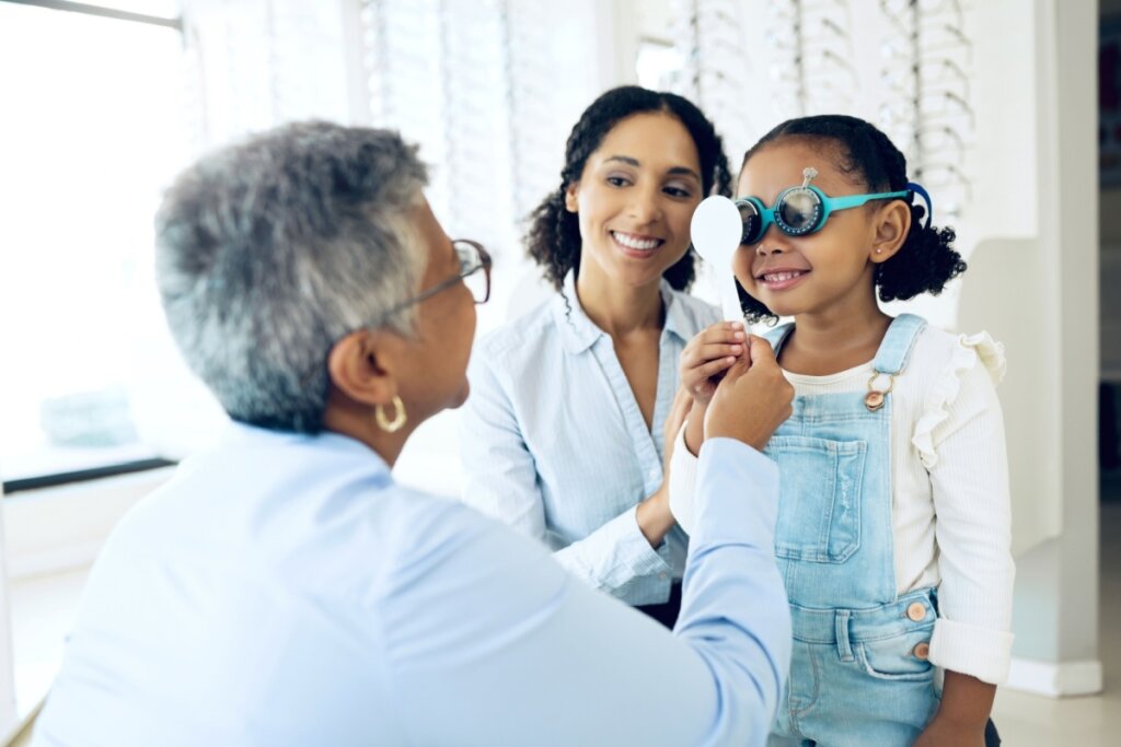 Menina realizando exame de vista com médica oftalma acompanhada da mãe.