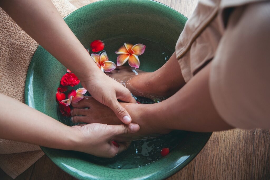Pés em compressa em uma bacia verde e uma mão fazendo massagem nele 