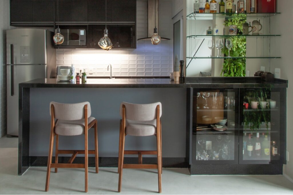 Cozinha integrada com bancada que funciona como bar, com banquetas, armários escuros e cristaleira lateral com garrafas e copos