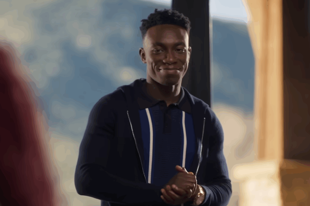 Homem jovem sorrindo de forma confiante em um ambiente interno, vestindo casaco