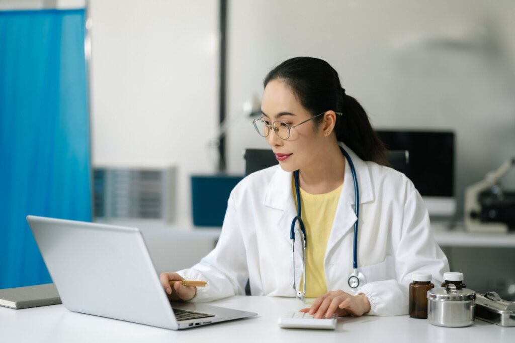 Médica de jaleco utilizando notebook e calculadora em consultório