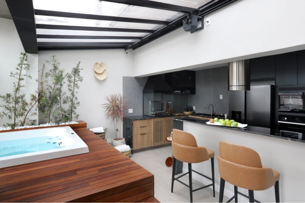 Área externa com cobertura de vidro, banheira branca e cadeira de couro na cor bege