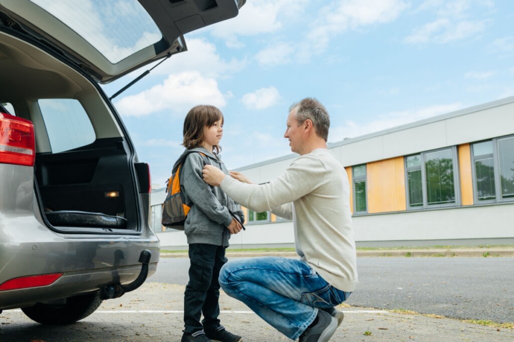 Homem agachado ajustando mochila de um menino