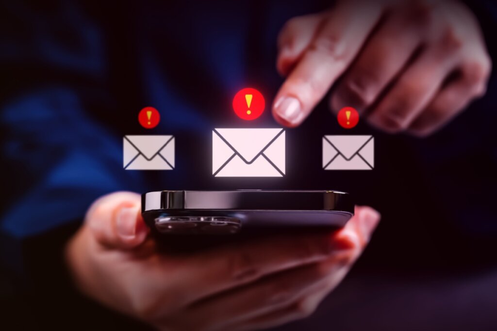 Mãos segurando um celular com a ilustração de três cartas com mensagens suspeitas em cima 