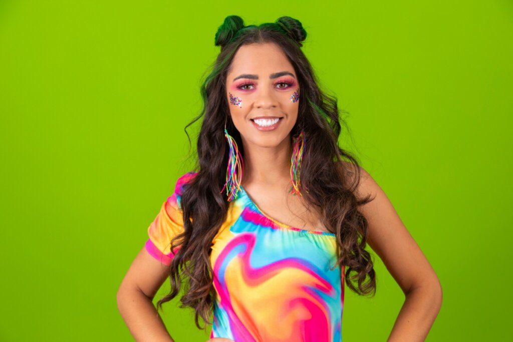 mulher de cabelo longo e ondulado, camiseta colorida e maquiagem com brilho no rosto