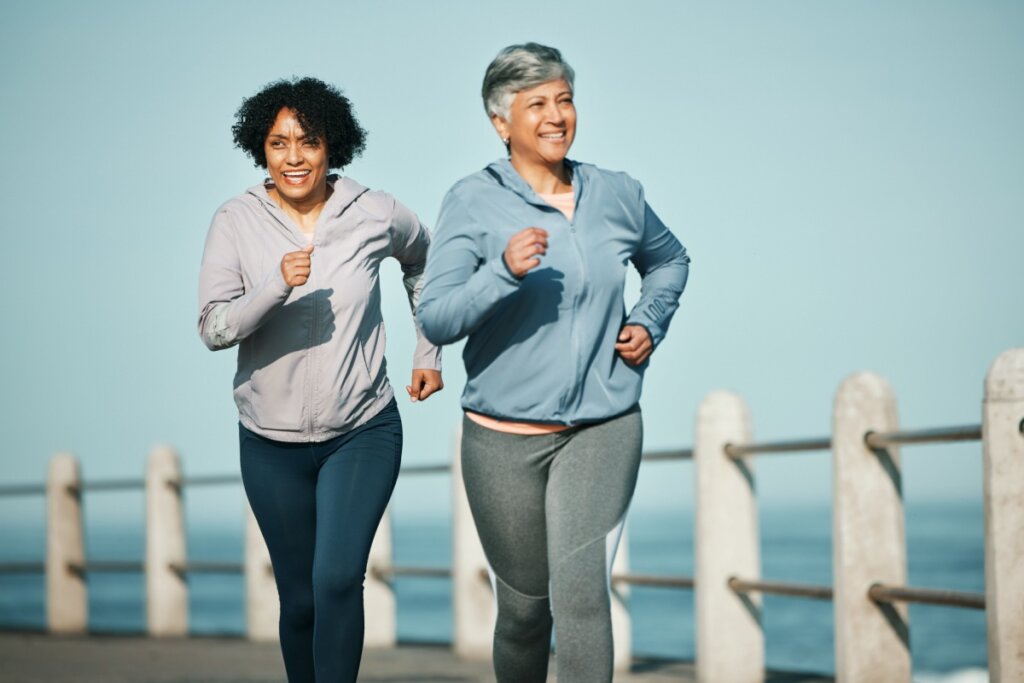 Duas senhoras com blusa de frio sorrindo e correndo em dia com céu azul
