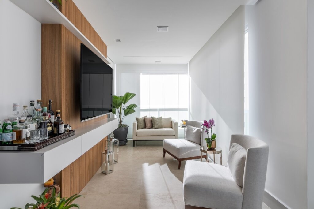 Varanda de estar com rack suspenso e bandeja de bar apoiada sobre o móvel próximo às poltronas