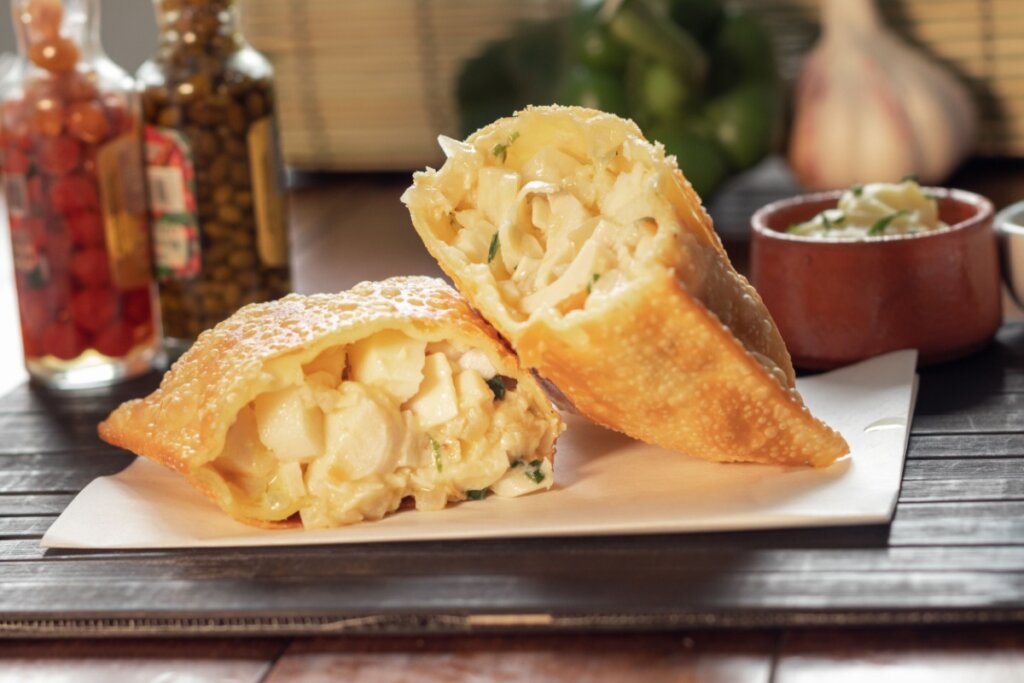 Pastel de palmito dividido em 2 em cima de papel em cima de mesa 