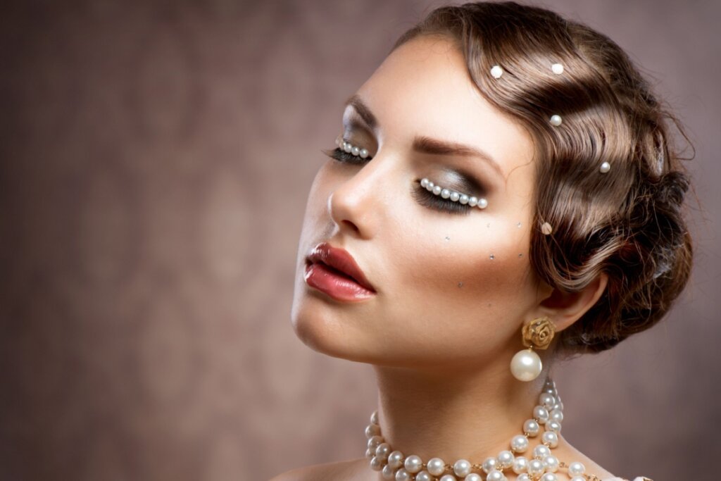 mulher de olhos fechados com pérolas coladas nos olhos e no cabelo. ela usa colar e brinco de pérola