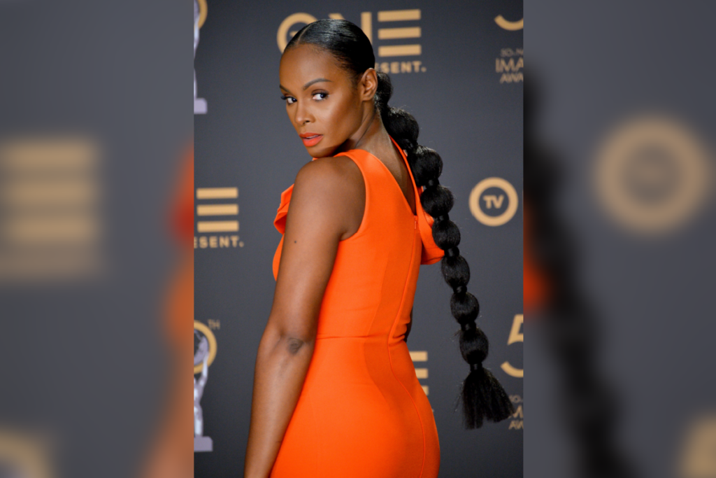 Mulher com cabelo com penteado bubble ponytail, usando vestido laranja, virada de costas  e olhando para trás 