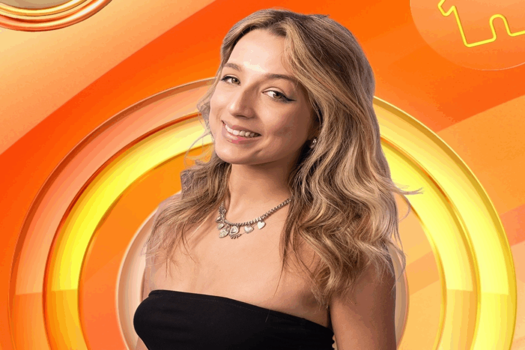 Mulher com o cabelo loiro ondulado, usando top preto em fundo com tons de laranja e amarelo