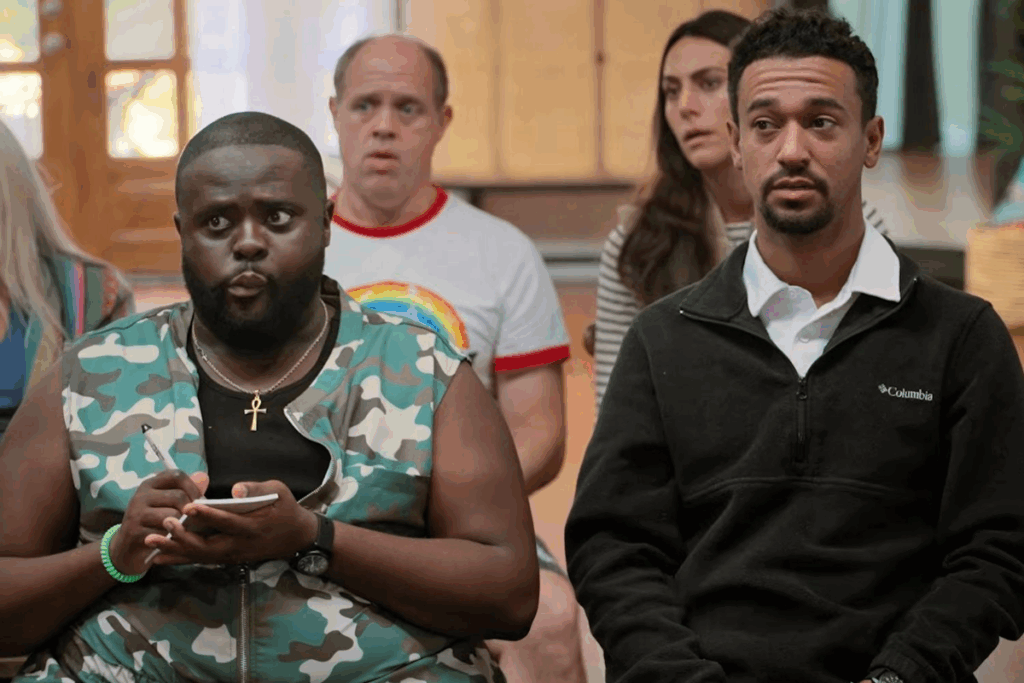 Imagem de três homens e uma mulher sentados assistindo palestra, um deles tem o cabelo curto, barba e está usando casaco preto, o outro tem o cabelo raspado e está usando uma regata estampada, o tem o cabelo curto e está usando camiseta branca com detalhes em vermelho e a mulher tem o cabelo longo e está usando camisa listrada branca e cinza