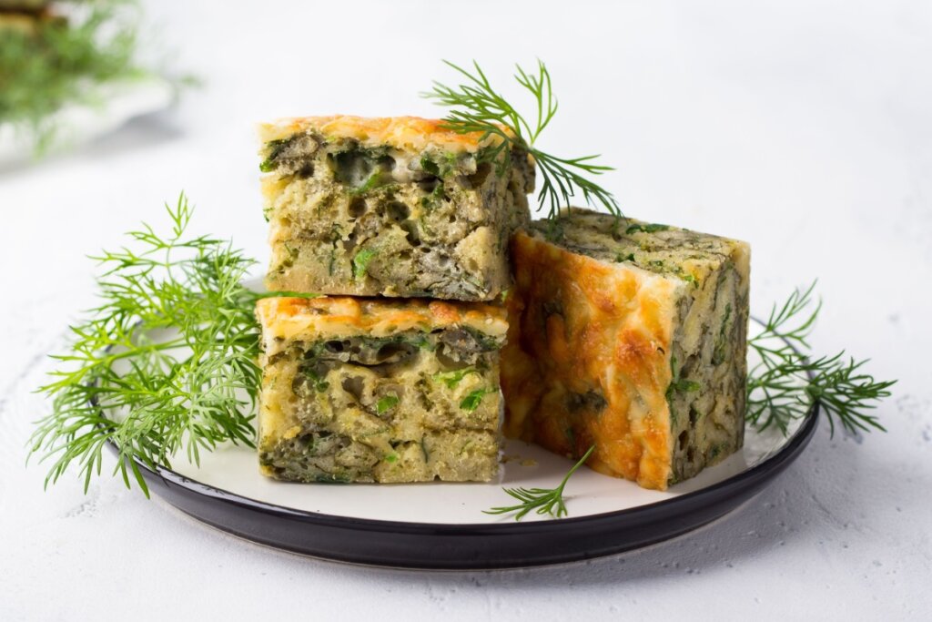 3 fatias de torta de abobrinha com espinafre servidas em prato branco em cima de bancada branca