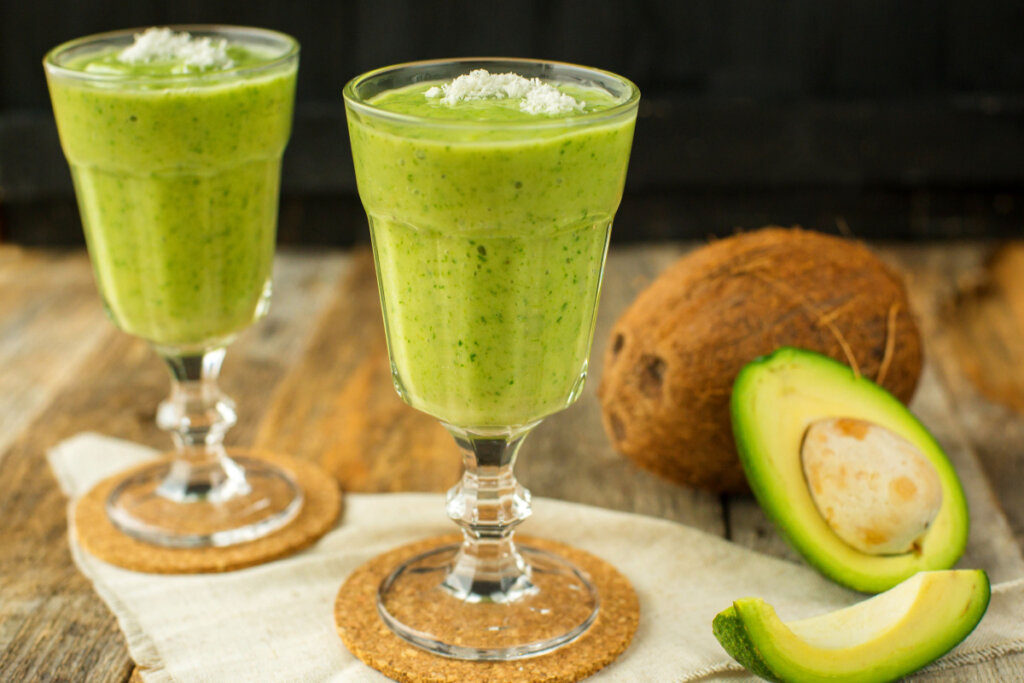 Vitamina de abacate com leite de coco em duas taças de vidro em cima de uma mesa de madeira