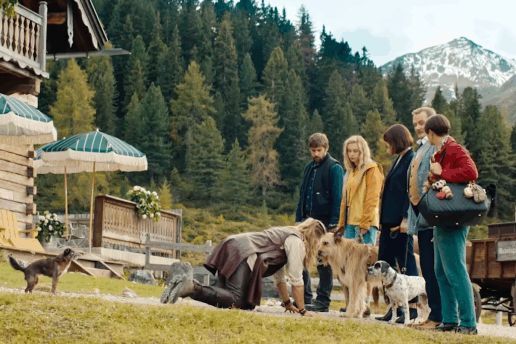Grupo de pessoas observando homem ajoelhado ao lado de cães em cenário montanhoso