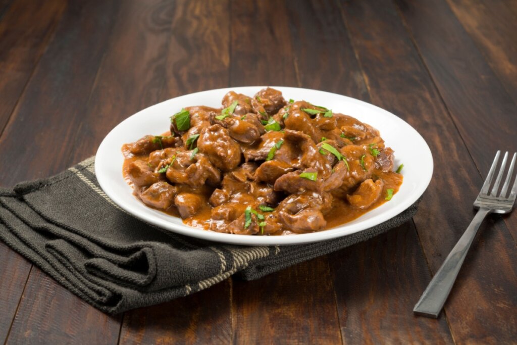 Prato branco com pedaços de moela ao molho e salsinha sobre uma mesa de madeira