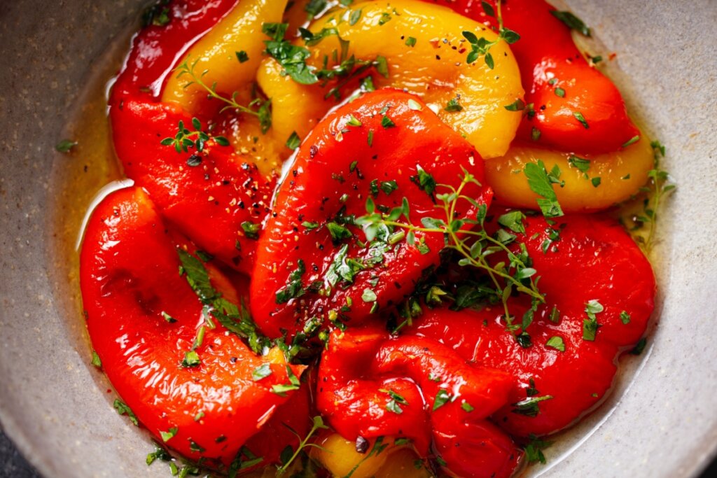Pimentões vermelhos e amarelos assados, envolvidos em azeite e ervas frescas