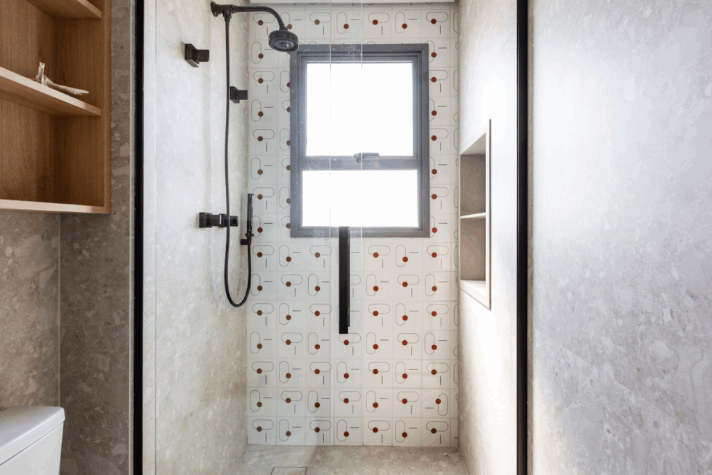 Banheiro com box iluminado por janela central e revestimento estampado com pequenos detalhes em destaque em vermelho e cinza