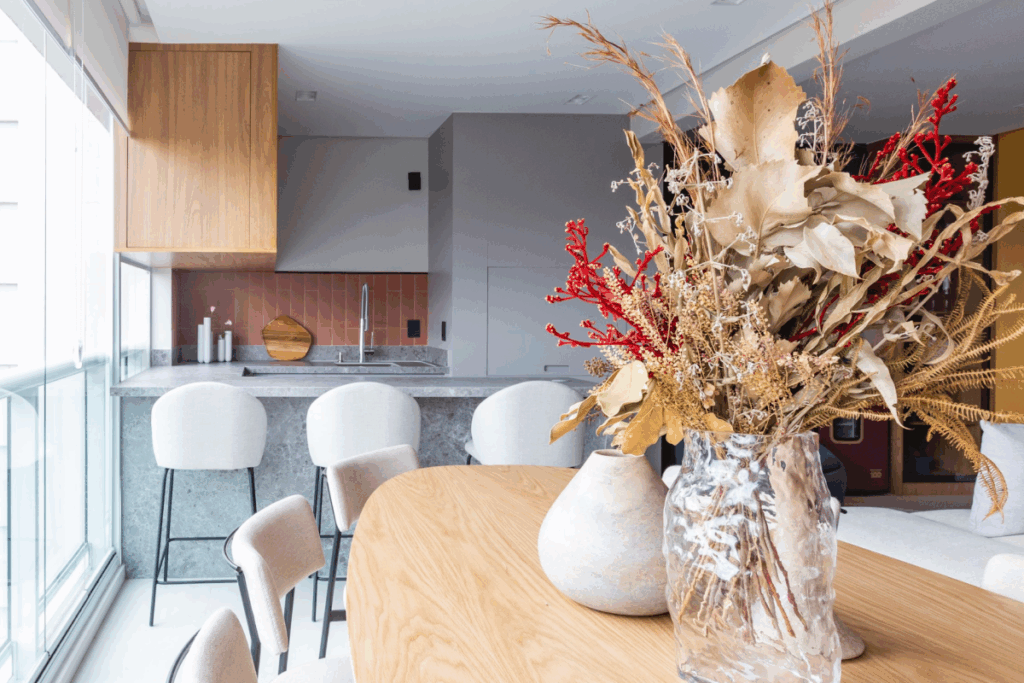 Espaço gourmet integrado com bancada em pedra, armários amadeirados e revestimento em tom rosado ao fundo