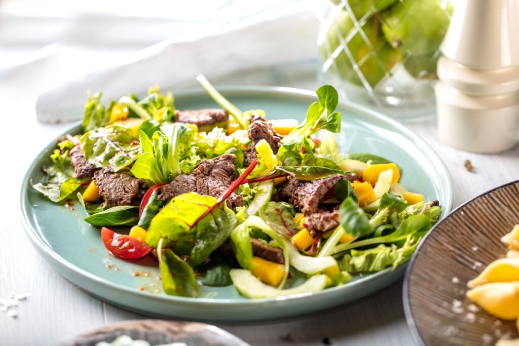 Salada com alface, rúcula e carne em um prato verde-claro