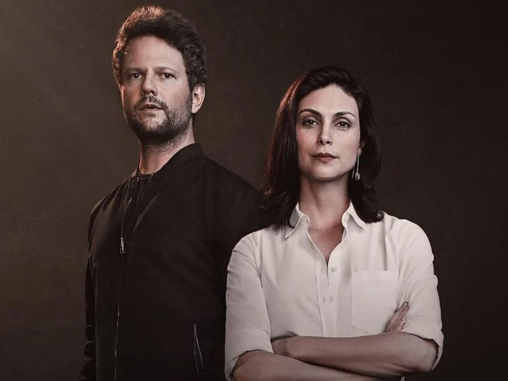 Retrato promocional da série "Sessão de Terapia". À esquerda, Selton Mello posa com uma expressão séria, vestindo uma jaqueta preta. À direita e levemente à frente, Morena Baccarin está com os braços cruzados, vestindo uma camisa social branca e exibindo um olhar confiante. O fundo é neutro em tons de marrom escuro, com uma iluminação dramática vinda da lateral que destaca os contornos dos rostos dos atores.