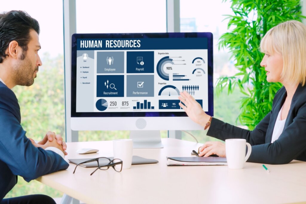 Duas pessoas sentadas e olhando para tela de um computador com dados do recursos humanos