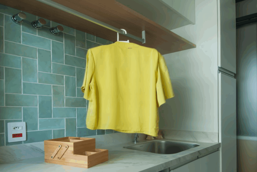 Área de serviço com revestimento verde em parede, bancada clara e peça de roupa amarela pendurada em cabide