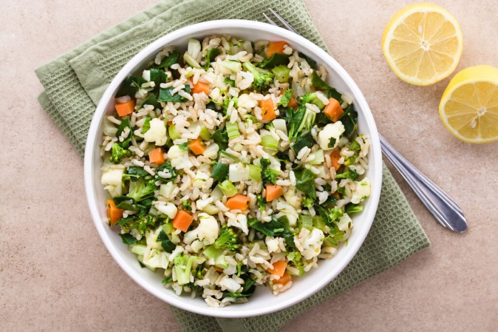 Arroz com acelga, cenoura e brócolis servido em tigela funda em cima de gurdanapo verde em cima de bancada de pedra