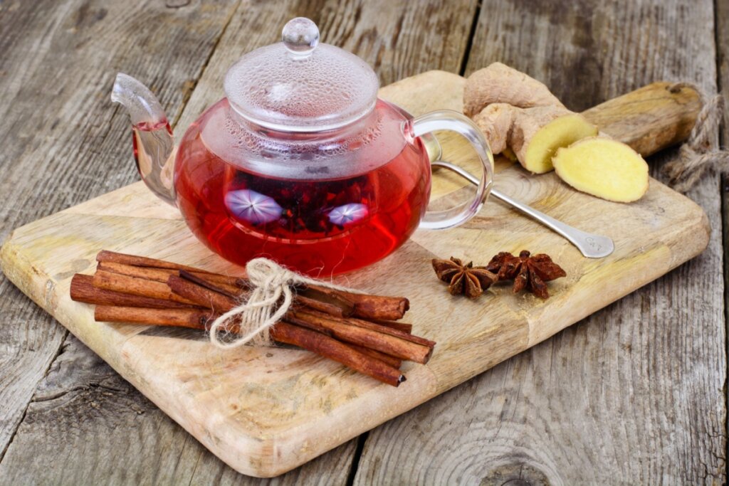 chaleira de vidro com chá vermelho. ela está em cima de tábua com canela, anis-estrelado e gengibre