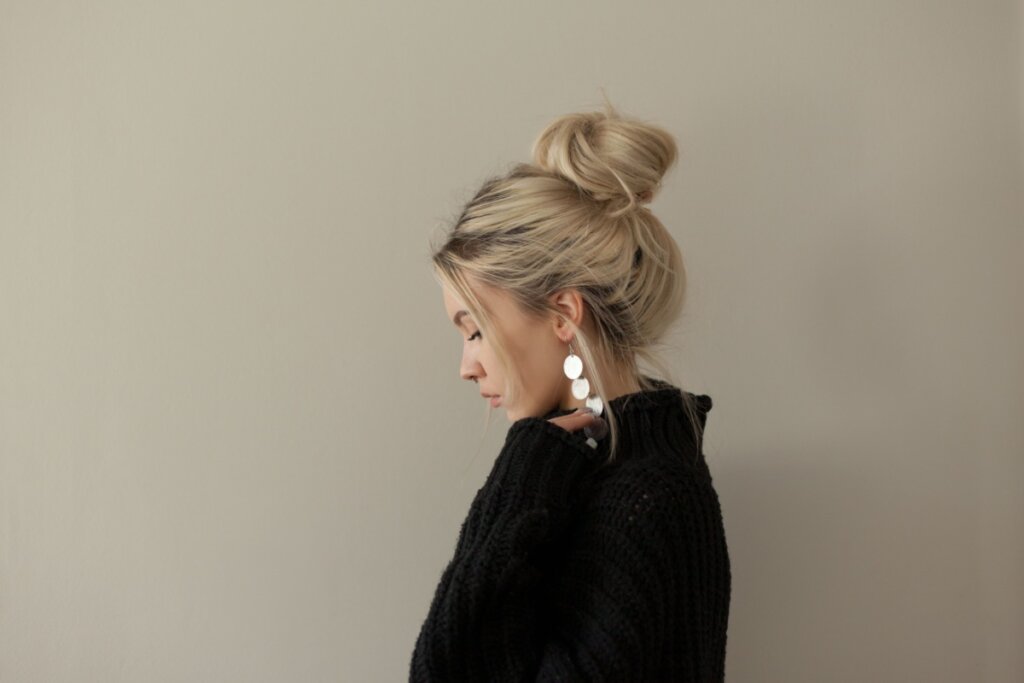 Mulher loira com o cabelo com coque despojado virada de lado e usando blusa preta 