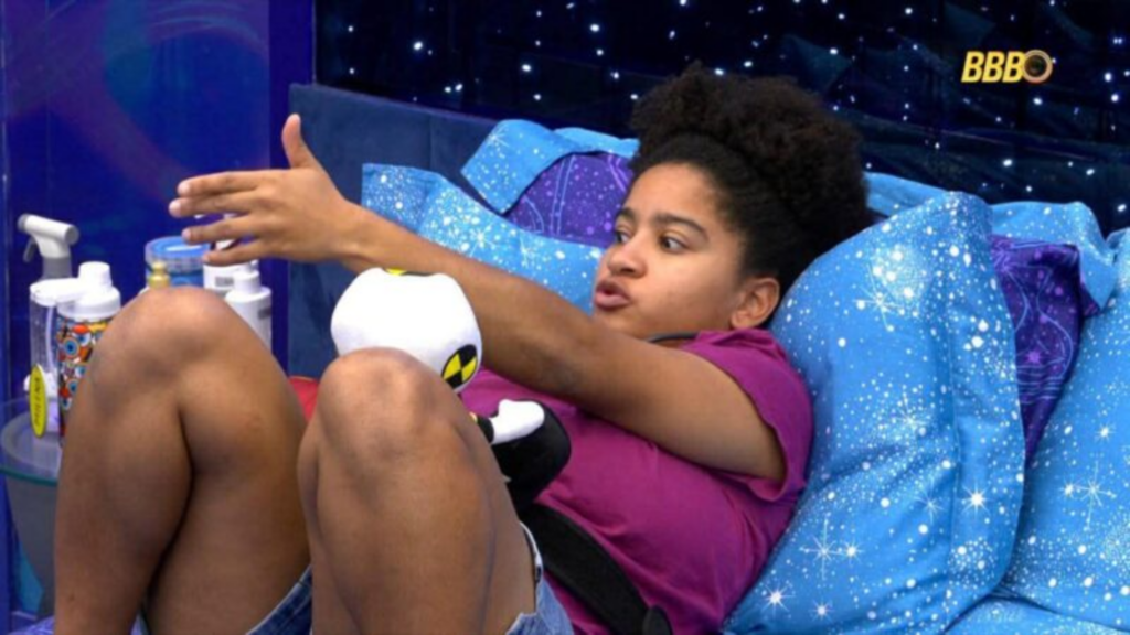 Milena deitada na cama apontando para a frente