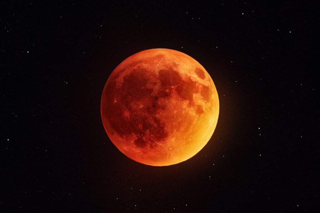 Fotografia centralizada da Lua cheia durante um eclipse lunar total, apresentando uma tonalidade avermelhada e alaranjada intensa, fenômeno conhecido como "Lua de Sangue".