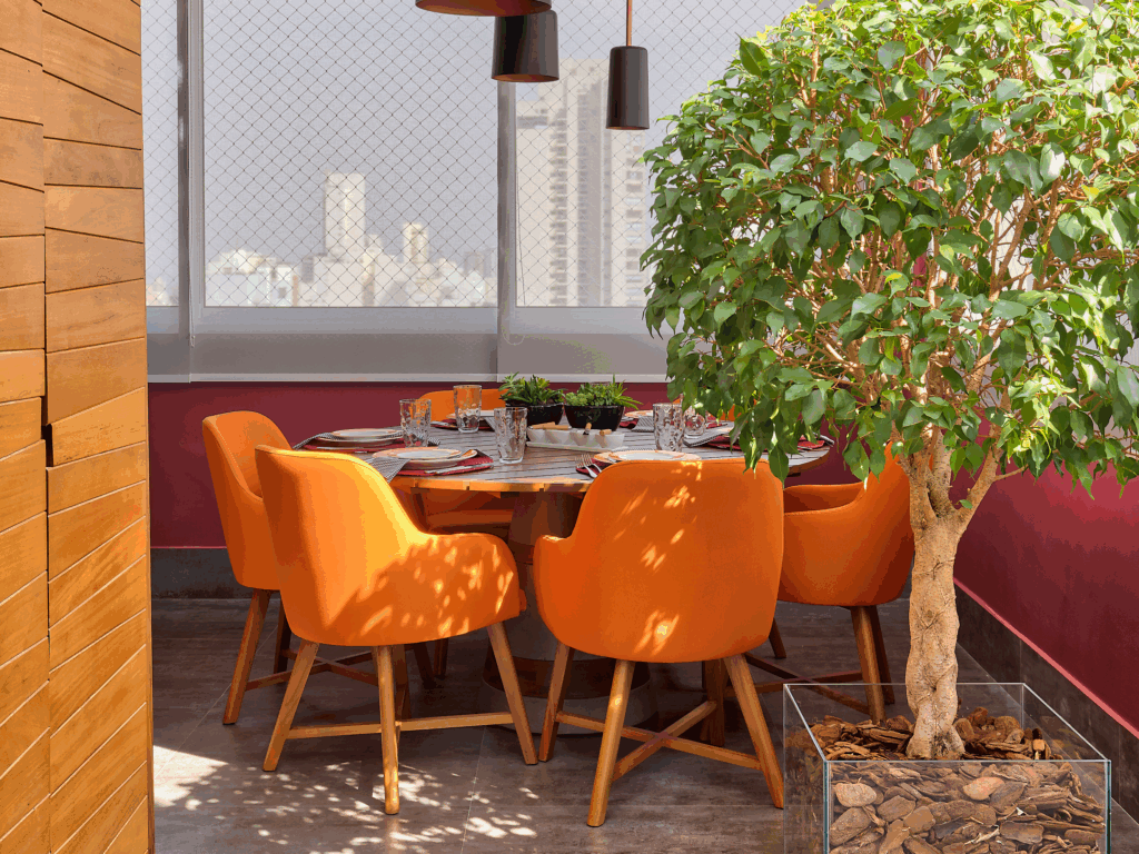 Mesa de jantar com cadeiras laranja e árvore ao lado