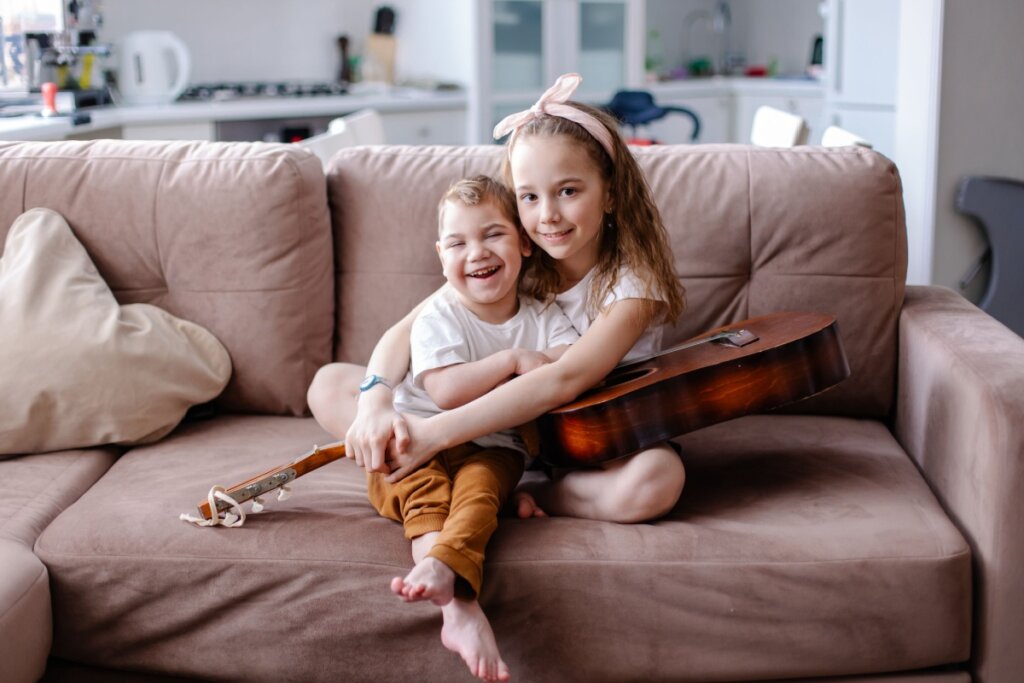 Menina e menino, sentados em um sofá e com violão no colo, abraçados