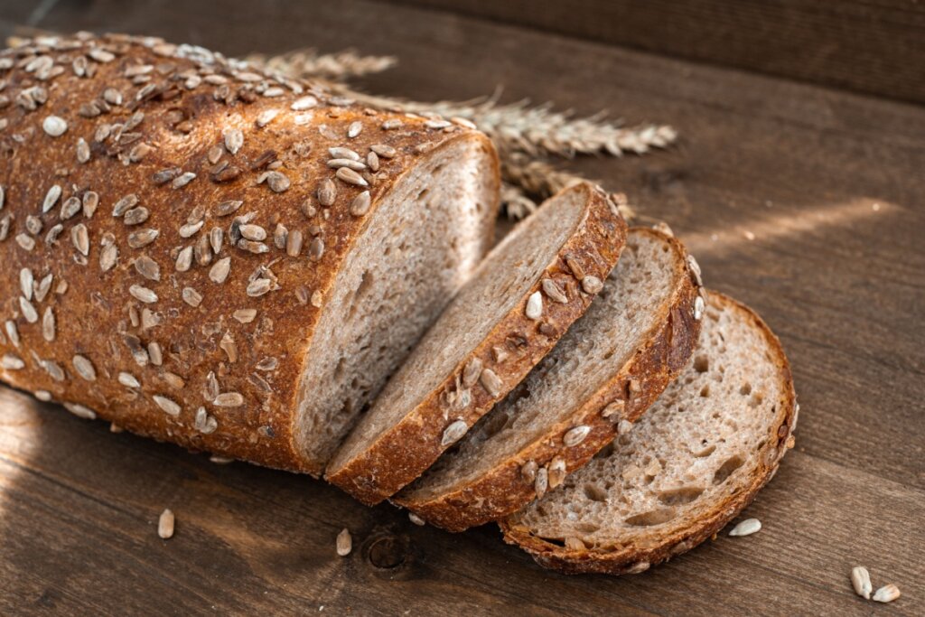 Pão integral com centeio e gergelim servido fatiado em cima de mesa de madeira 