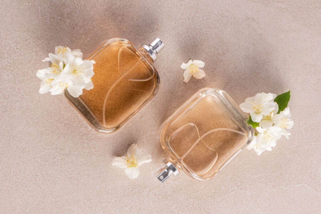 Frascos de perfume de vidro com flores de jasmim ao lado em cima de bancada bege