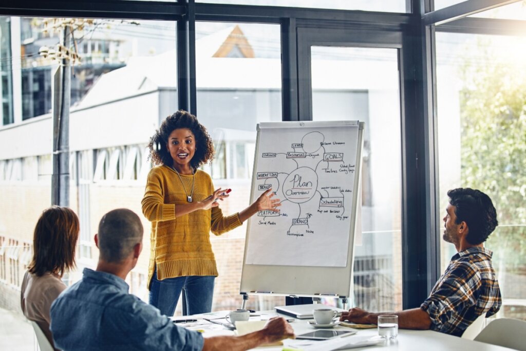 Mulher palestrando para três pessoas sentadas em uma mesa 