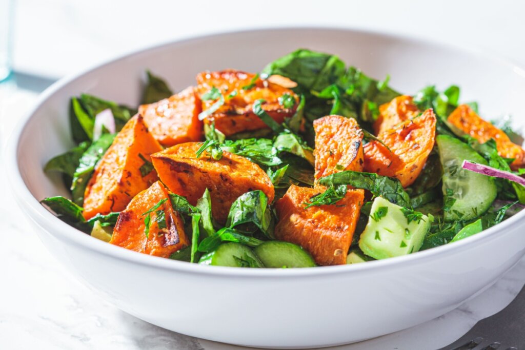 recipiente branco com salada de batata-doce com folhas verdes e pepino 