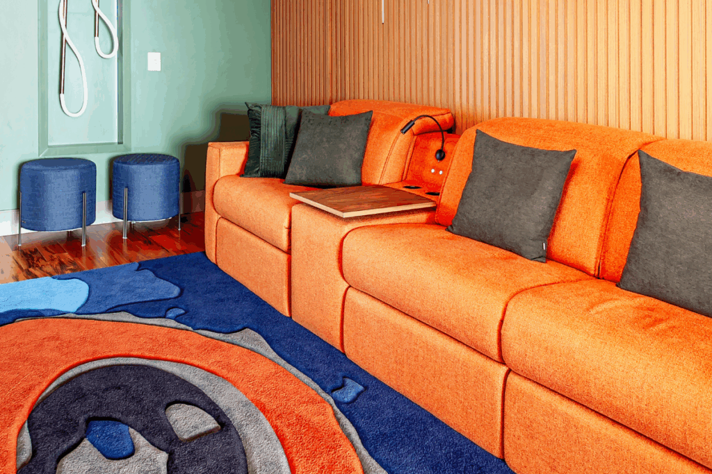 Sala com parede em madeira, sofá laranja e almofadas marrom e verde com tapete azul, laranja e cinza