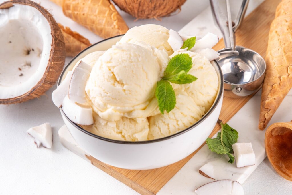 Sorvete de coco cremoso  servido em tigela funda branca em formato de bolas em cima de bancada branca