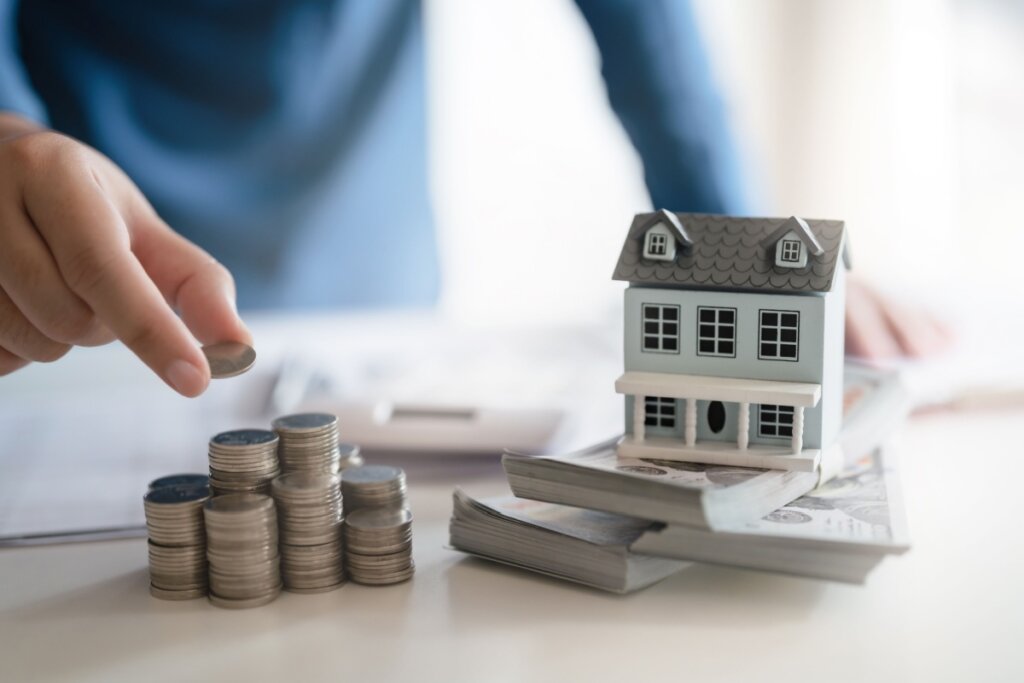 Miniatura de casa ao lado de moedas empilhadas