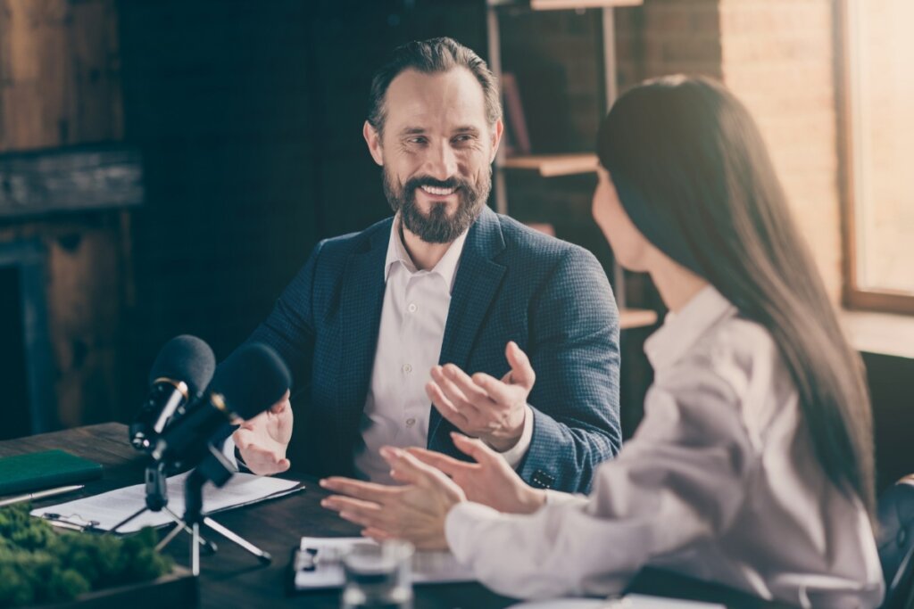 Homem e mulher sentados conversando em frente a dois microfones