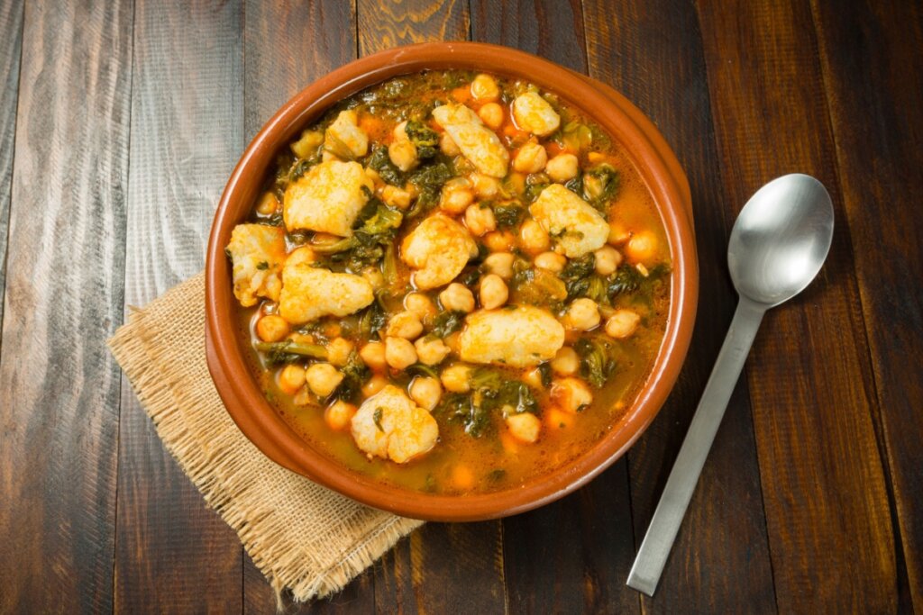 Sopa de grão-de-bico com bacalhau e espinafre servida em tigela rústica sobre mesa de madeira com colher ao lado