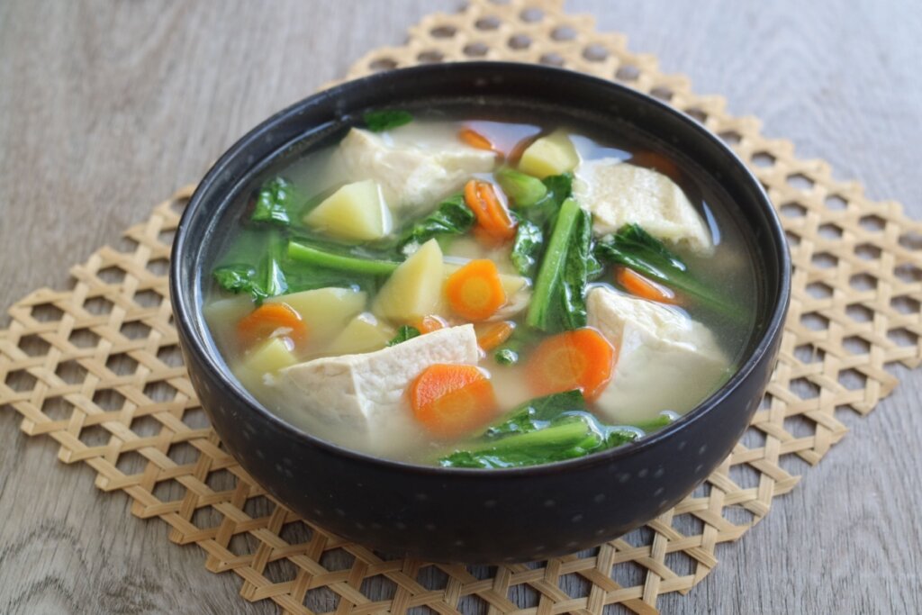 Recipiente preto com sopa de vegetais com tofu